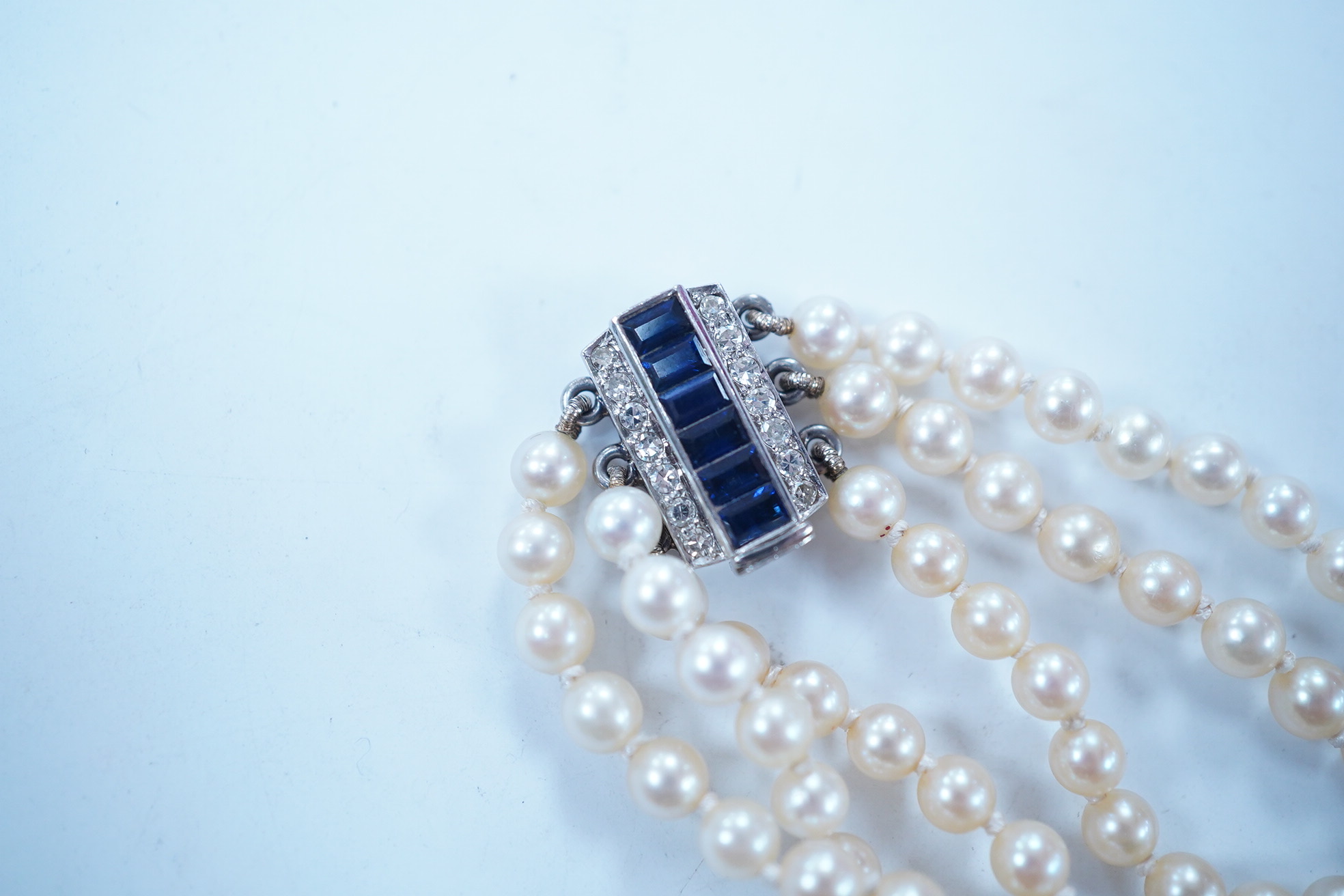 A triple strand cultured pearl choker necklace, with sapphire and diamond cluster set rectangular white metal clasp, 32cm. Condition - fair to good